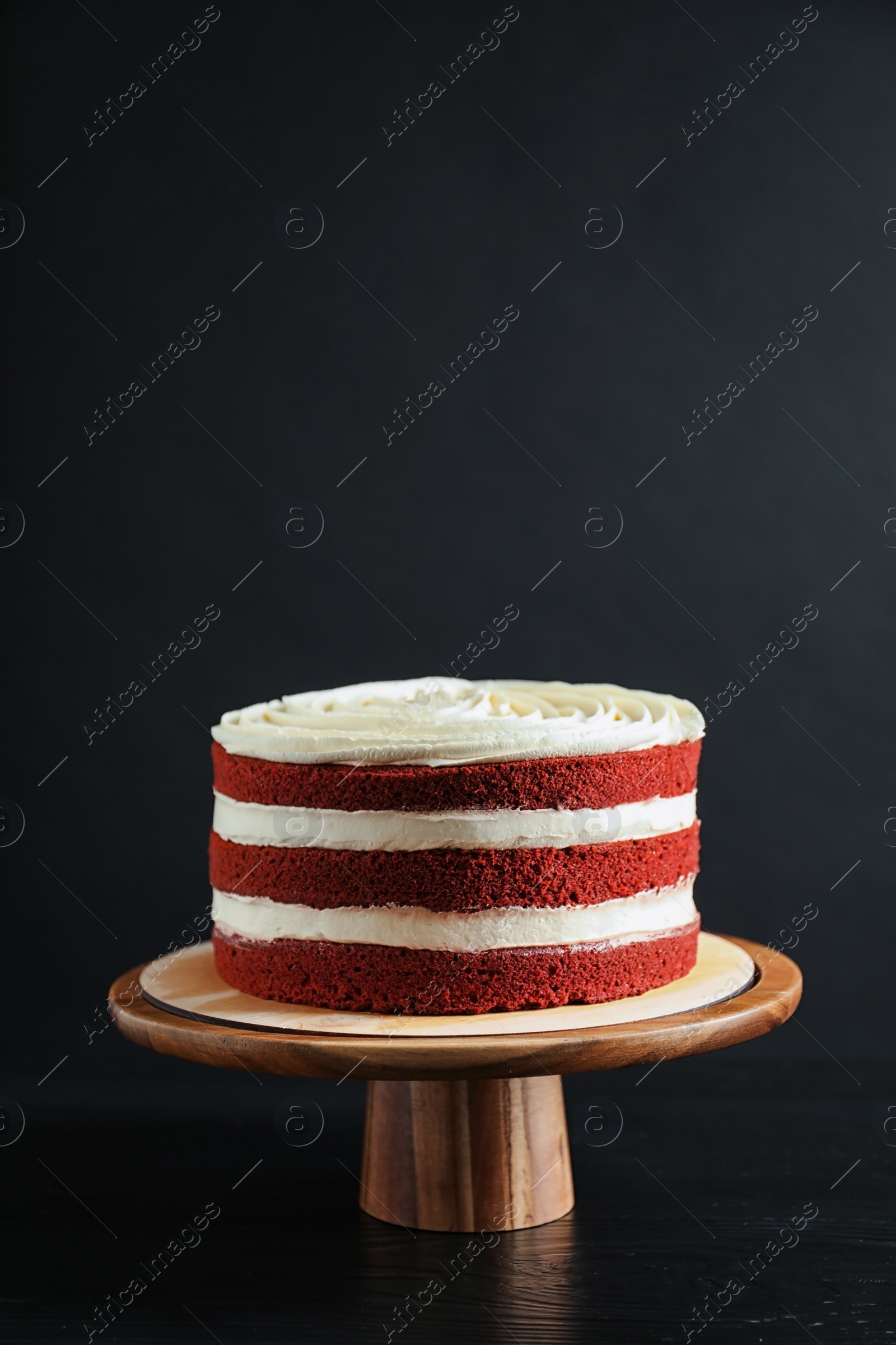 Photo of Delicious homemade red velvet cake on wooden stand against black background