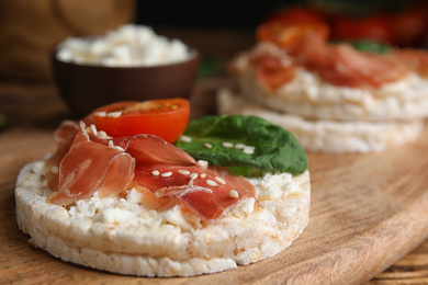 Photo of Puffed rice cake with prosciutto, tomato and basil on wooden board, closeup
