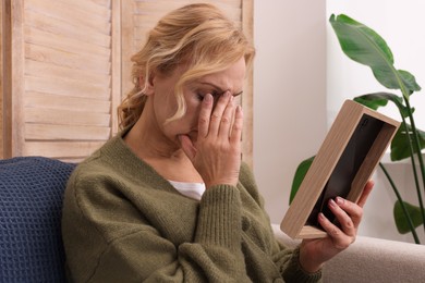 Upset middle aged woman with photo frame at home. Loneliness concept