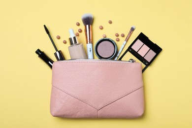 Cosmetic bag with makeup products and accessories on yellow background, flat lay