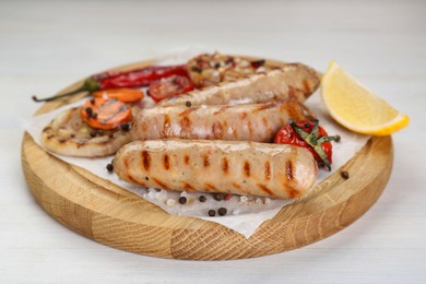 Photo of Tasty grilled sausages with vegetables, lemon and spices on white wooden table, closeup
