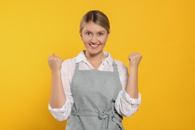 Photo of Beautiful young woman in clean apron with pattern on orange background