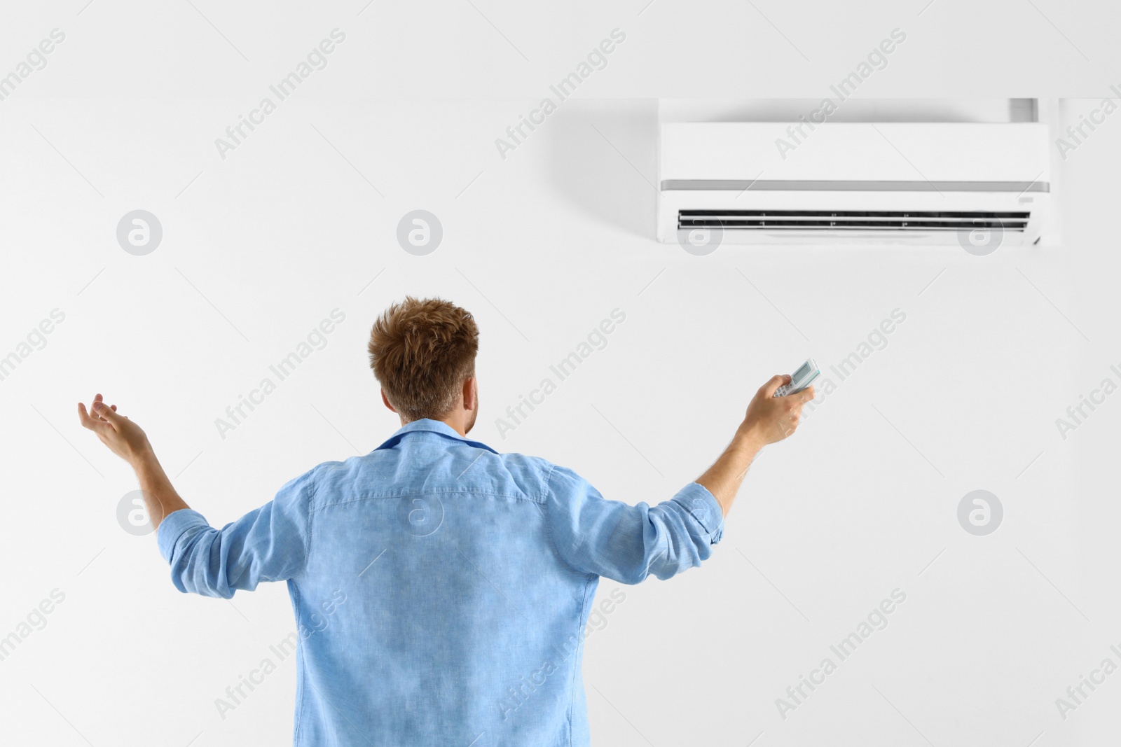 Photo of Young man operating air conditioner with remote control indoors