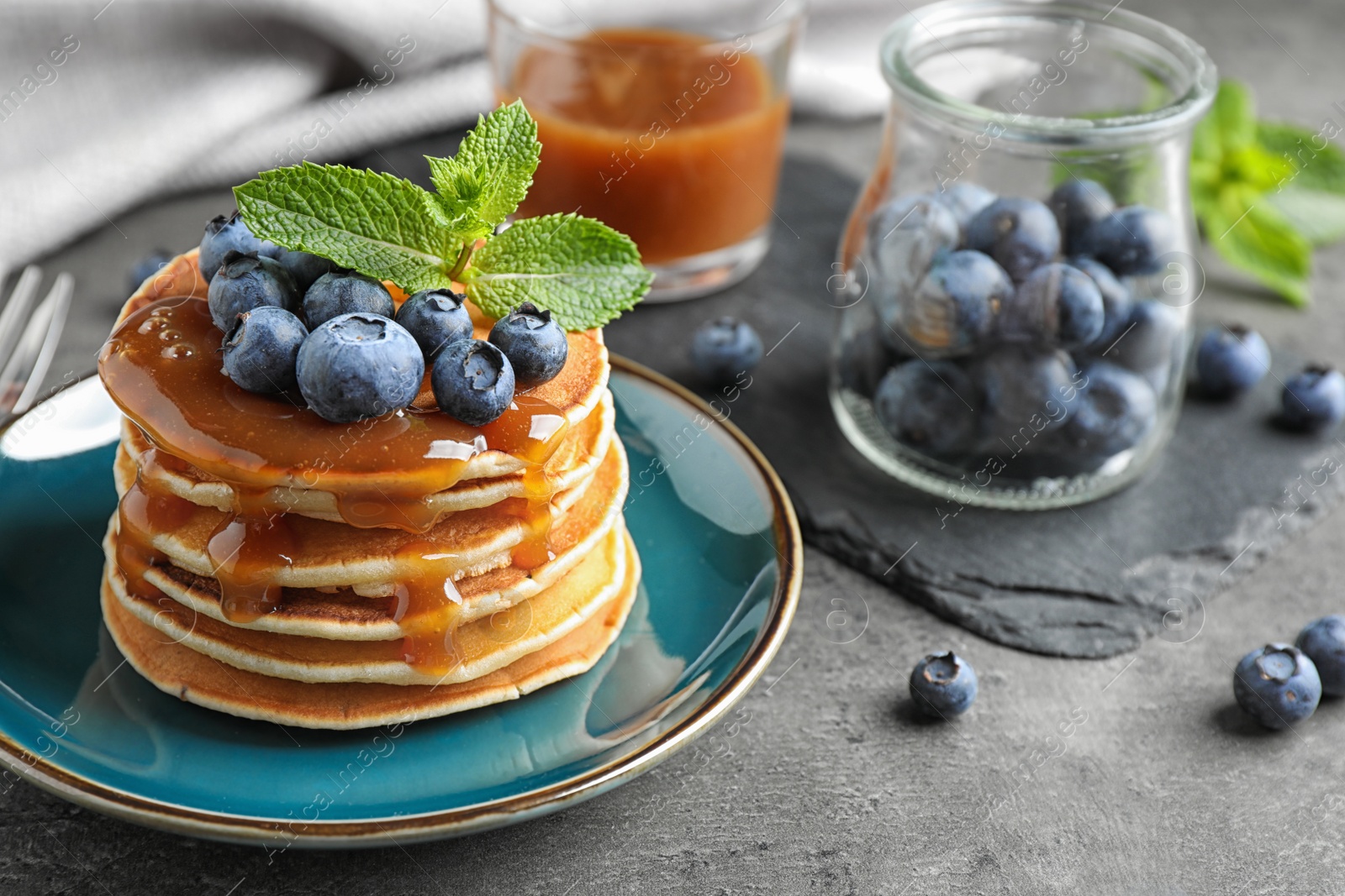 Photo of Delicious pancakes with fresh blueberries and syrup on grey table