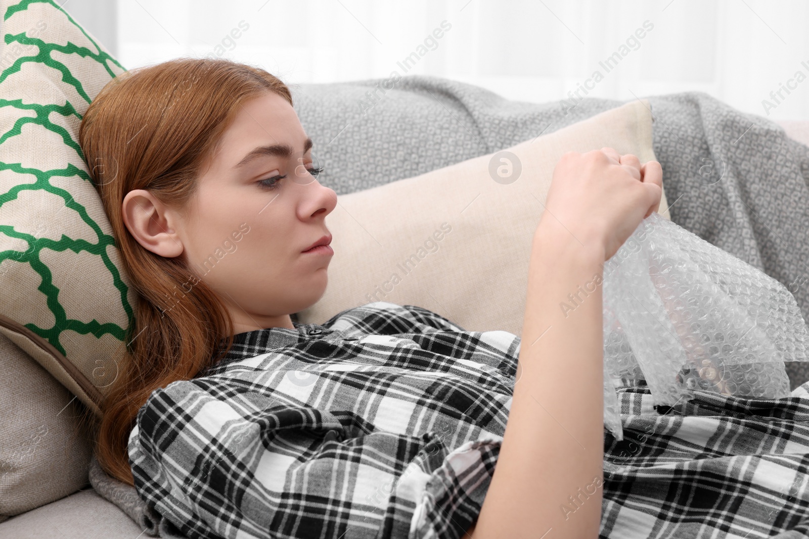 Photo of Sad woman popping bubble wrap on sofa at home. Stress relief