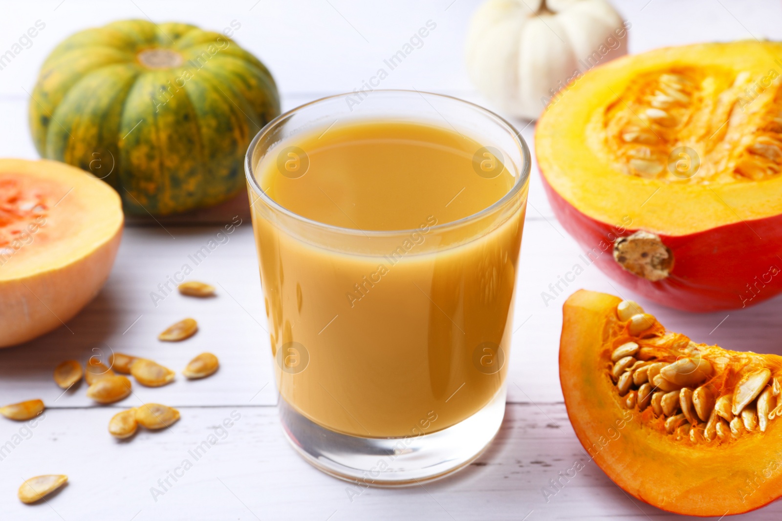 Photo of Tasty pumpkin juice in glass and different pumpkins on white wooden table