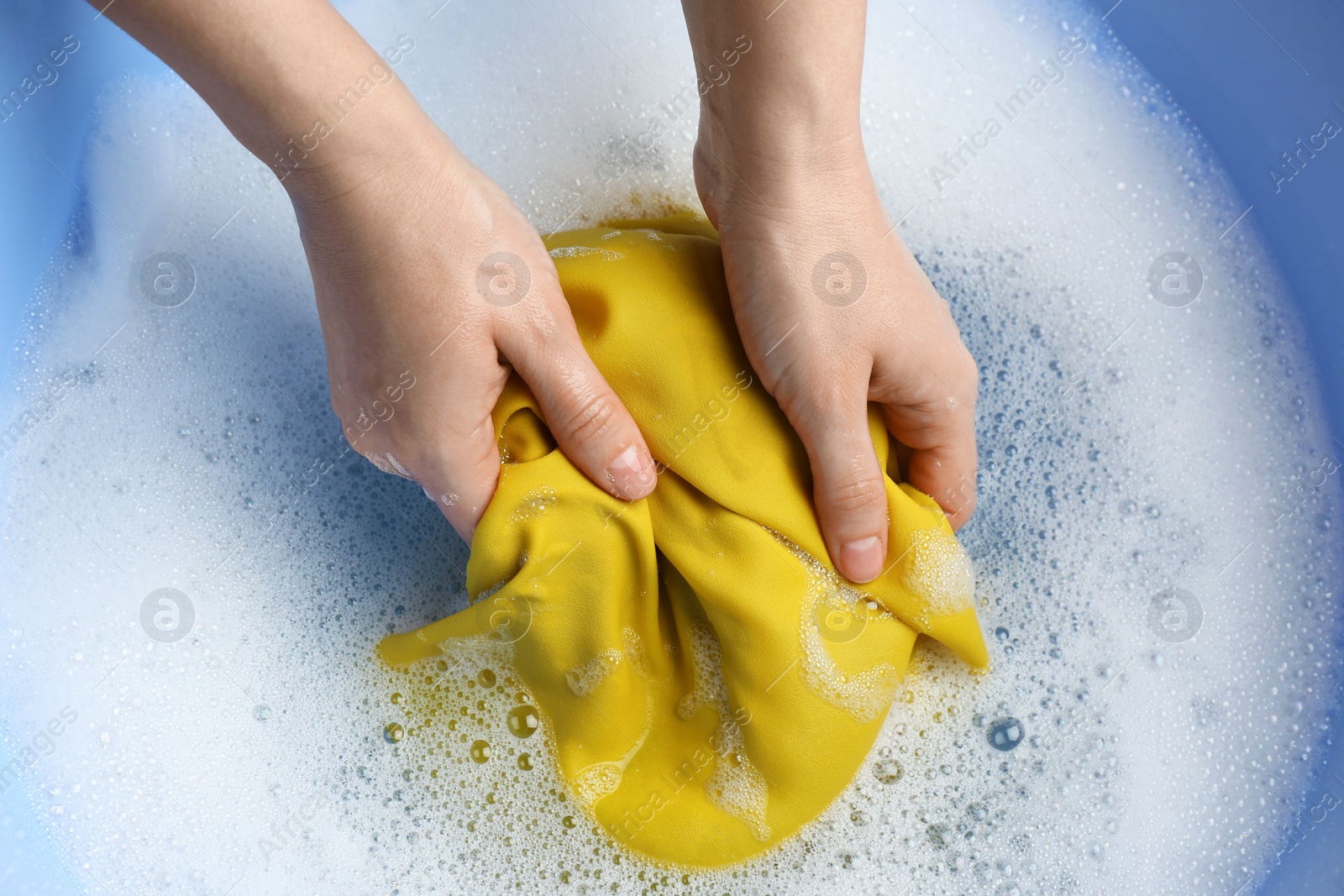 Photo of Top view of woman hand washing color clothing in suds, closeup