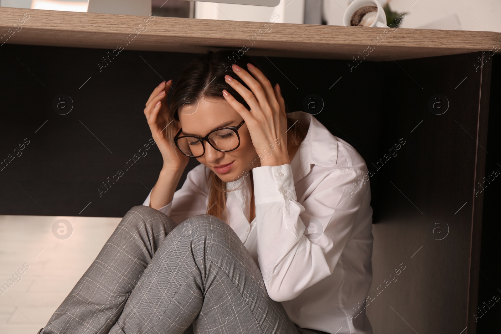 Photo of Scared young woman hiding under office desk during earthquake