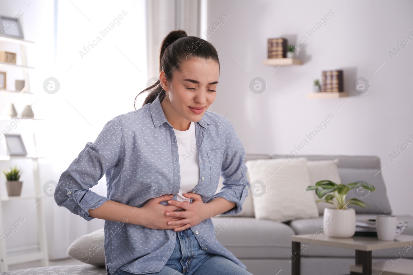 Photo of Young woman suffering from stomach ache at home. Food poisoning