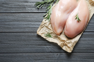 Photo of Parchment with raw chicken breasts and rosemary on wooden background, top view. Space for text