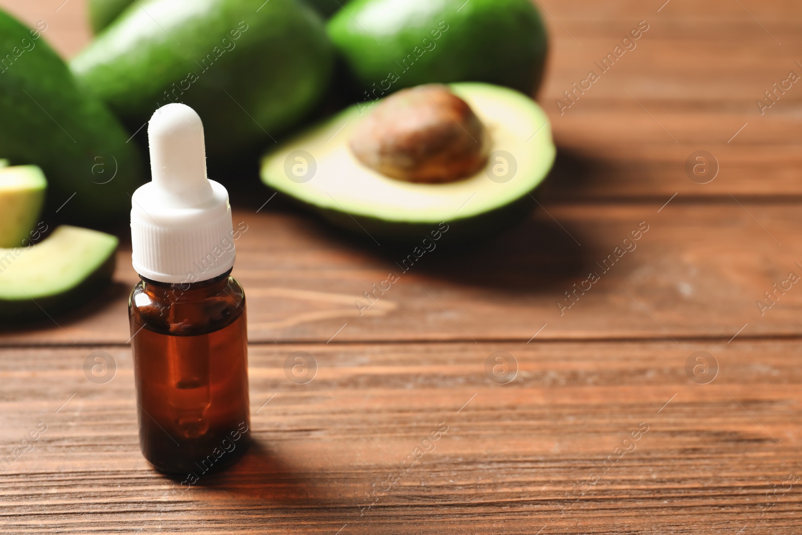 Photo of Bottle with oil and fresh avocados on wooden table