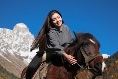 Photo of Young woman riding horse in mountains on sunny day. Beautiful pet