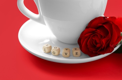 Photo of Cup of coffee, mini cubes with word LOVE and rose on red background, closeup