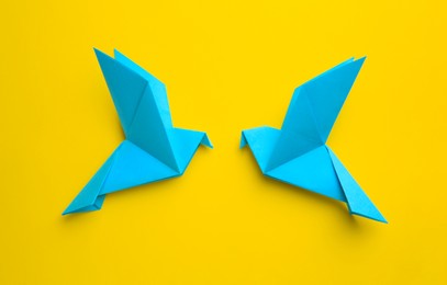 Photo of Origami art. Colorful handmade paper birds on yellow background, flat lay