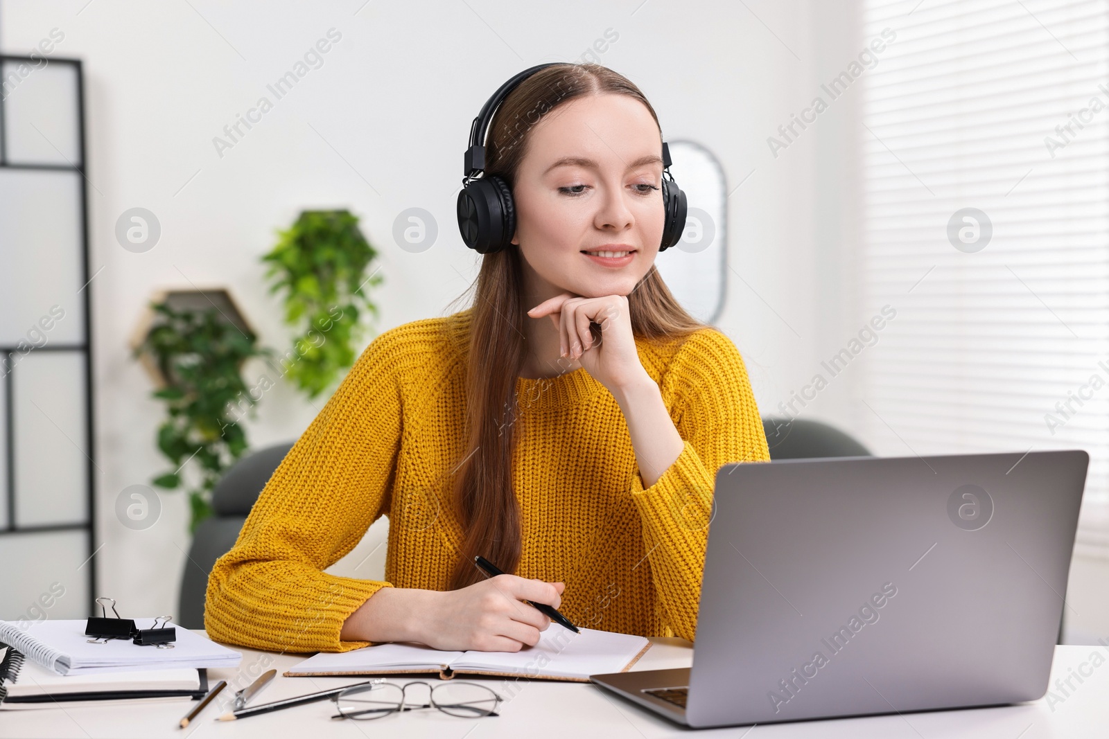 Photo of E-learning. Young woman using laptop during online lesson at white table indoors