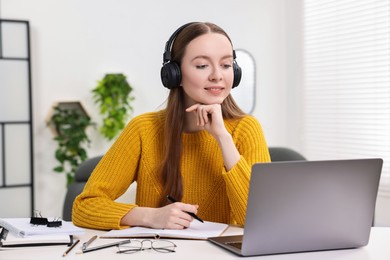 E-learning. Young woman using laptop during online lesson at white table indoors