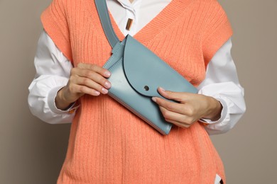 Young woman with stylish waist bag on grey background, closeup