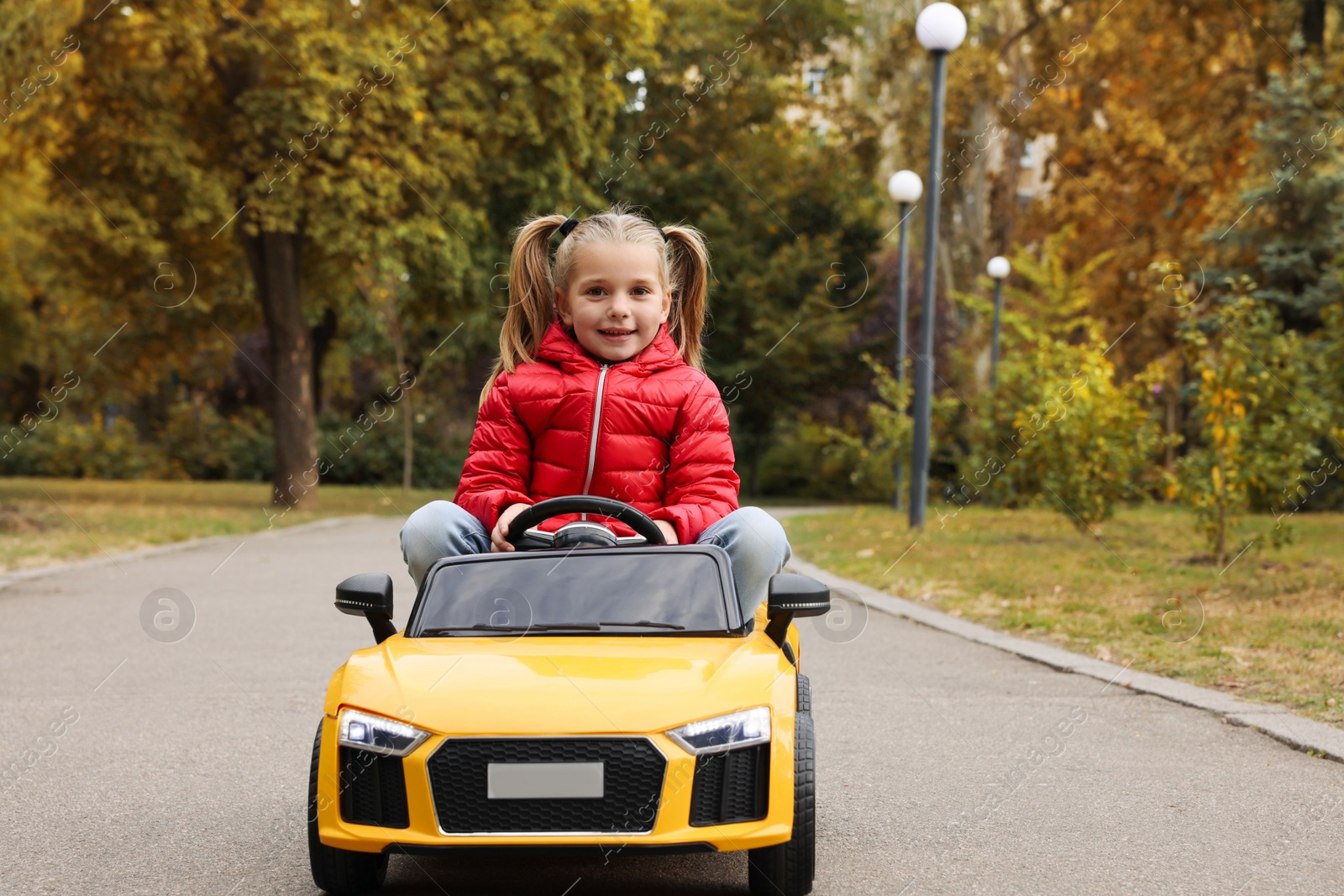 Photo of Cute little girl driving children's car outdoors