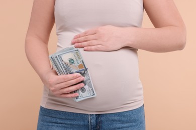 Photo of Surrogate mother. Pregnant woman with dollar banknotes on beige background, closeup