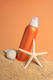 Sand with bottle of sunscreen, starfish and stones against orange background. Sun protection