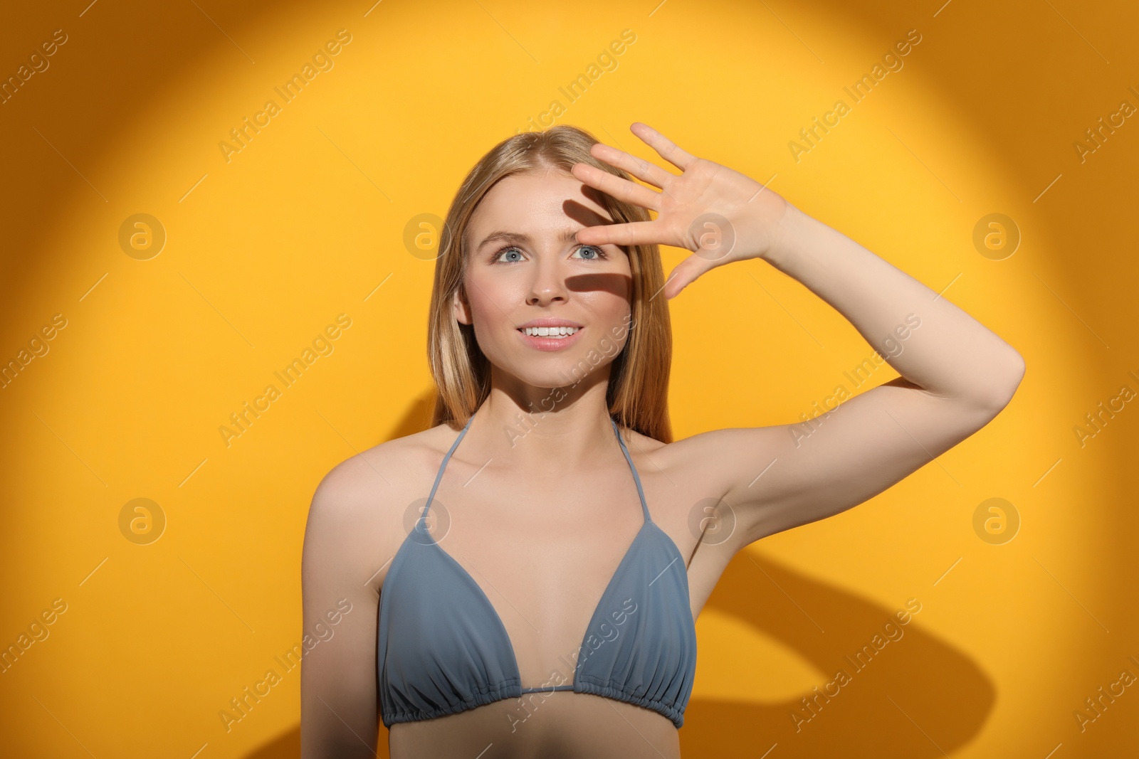 Photo of Beautiful young woman shading herself with hand from sunlight on orange background