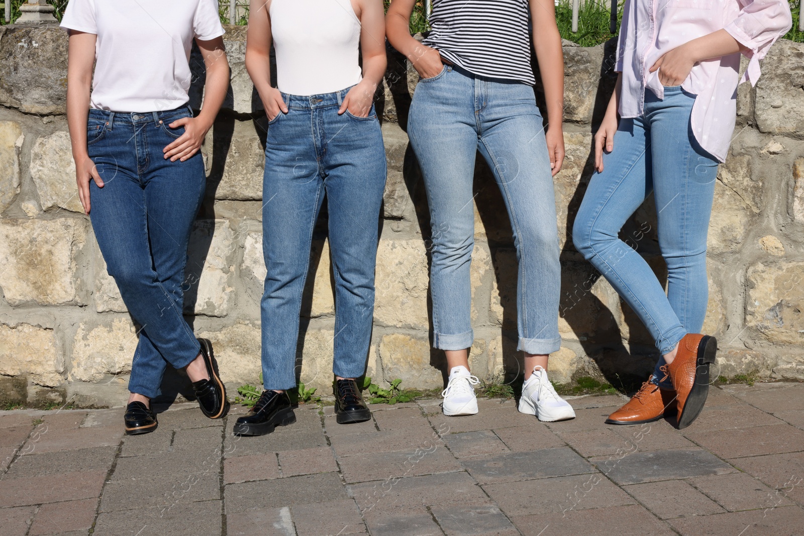 Photo of Women in stylish jeans near stone wall outdoors on sunny day, closeup