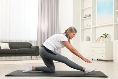 Photo of Happy senior woman practicing yoga on mat at home