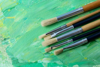 Set of different brushes on abstract colorful paint, flat lay