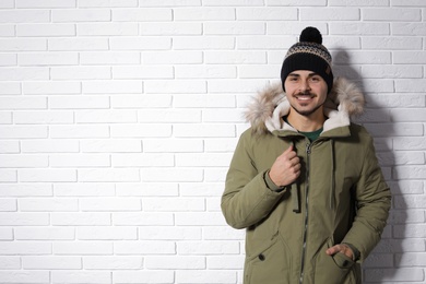 Photo of Young man wearing warm clothes against brick wall, space for text. Ready for winter vacation