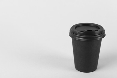 Black paper cup with plastic lid on light background, space for text. Coffee to go