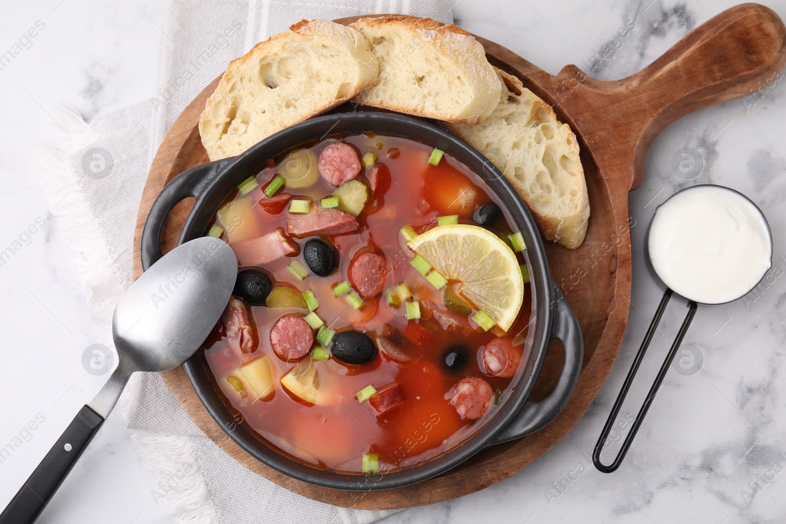 Photo of Meat solyanka soup with thin dry smoked sausages served on white marble table, flat lay