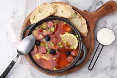 Photo of Meat solyanka soup with thin dry smoked sausages served on white marble table, flat lay