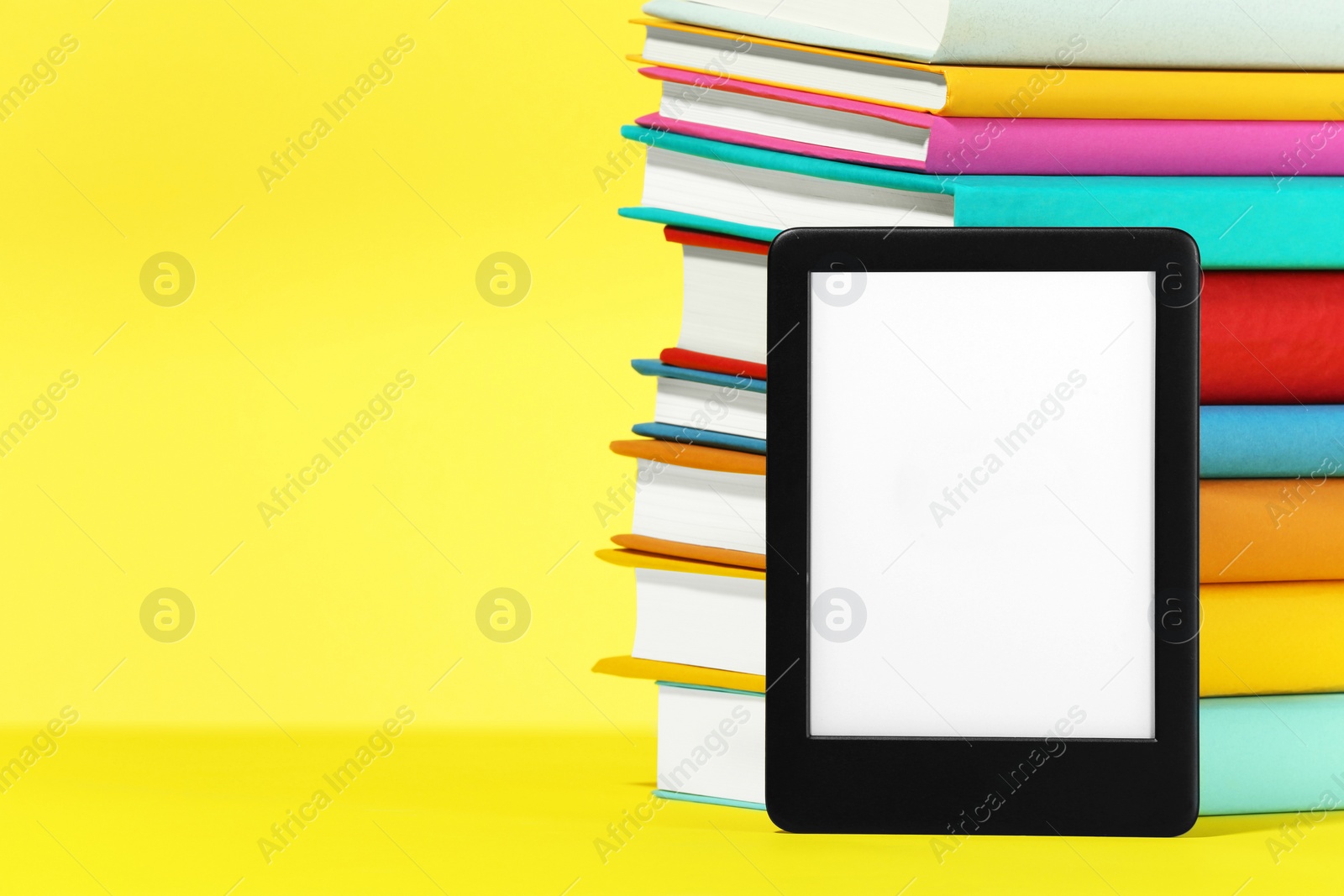 Photo of Modern e-book reader and stack of hard cover books on yellow background. Space for text