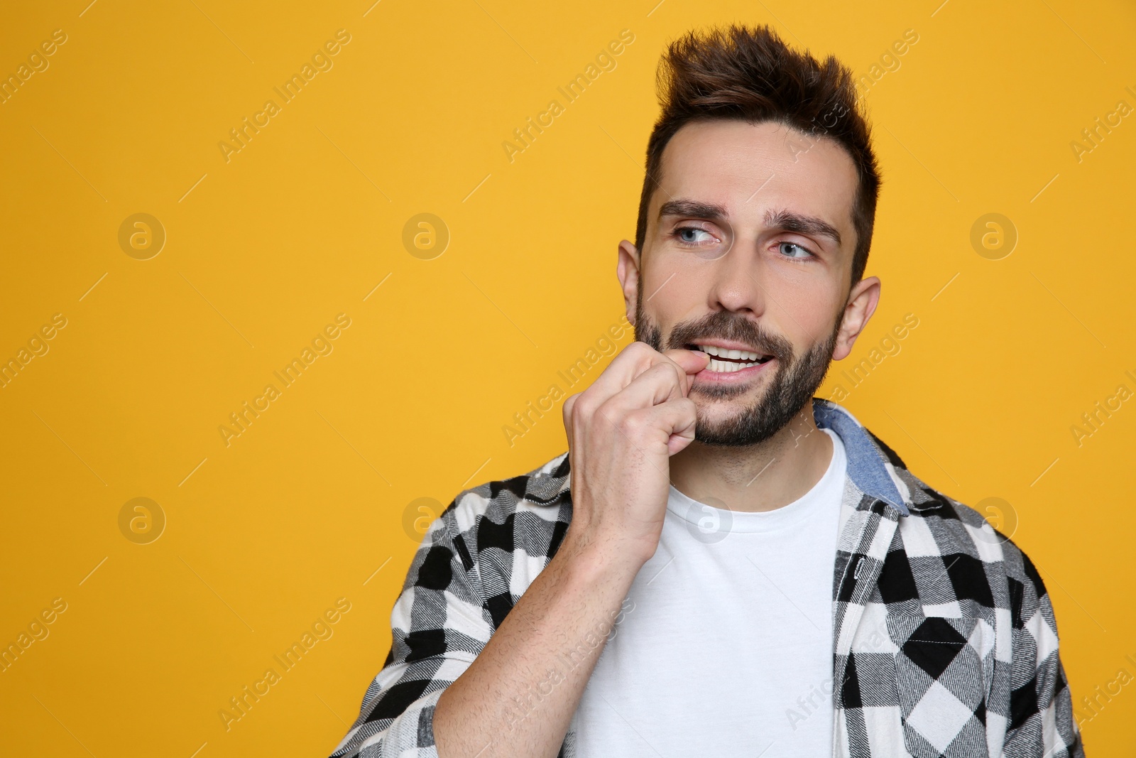 Photo of Man biting his nails on yellow background. Space for text