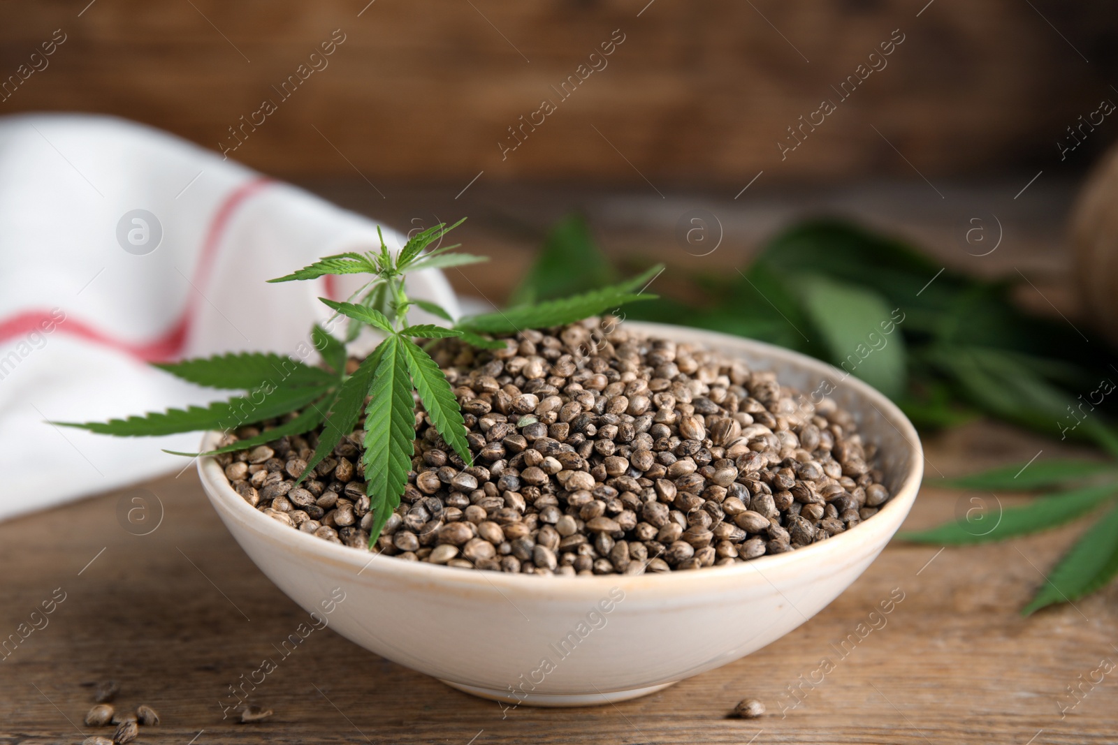 Photo of Bowl with hemp seeds and leaves on wooden table