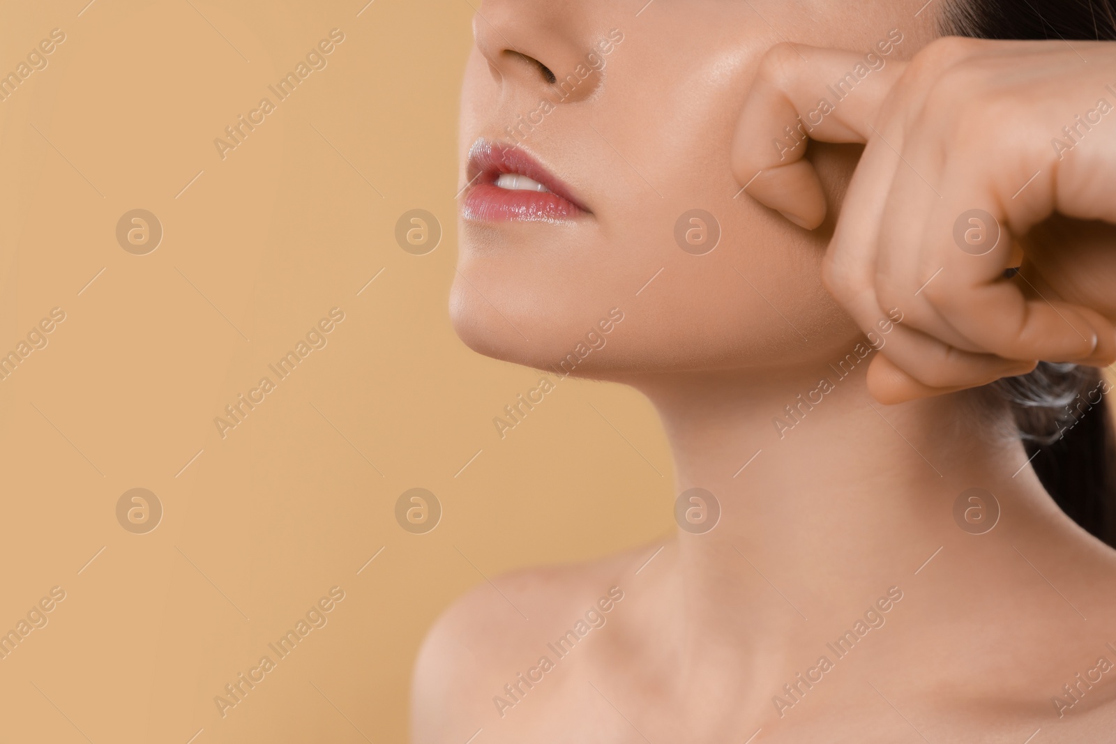 Photo of Young woman massaging her face on beige background, closeup. Space for text