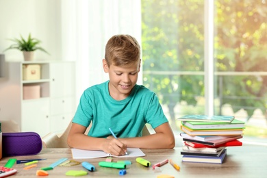 Photo of Cute boy doing homework at table with school stationery indoors