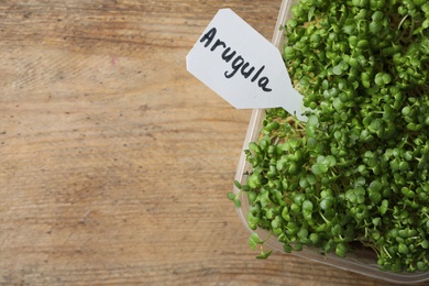 Sprouted arugula seeds in plastic container on wooden table, top view. Space for text