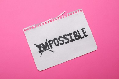 Photo of Motivation concept. Paper with changed word from Impossible into Possible by crossing over letters I and M on pink background, top view
