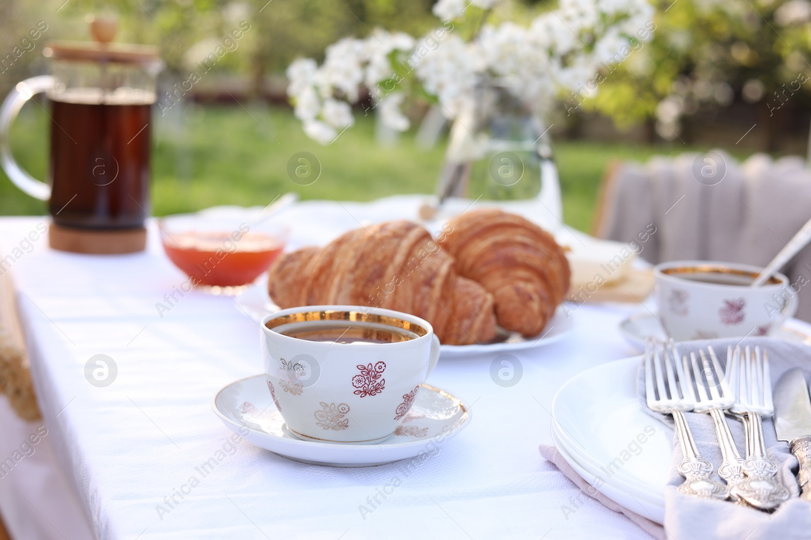 Photo of Stylish table setting with tea and croissants in spring garden