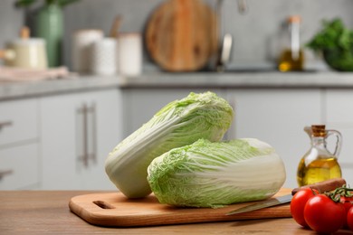 Photo of Fresh Chinese cabbages, knife, tomatoes and oil on wooden table in kitchen