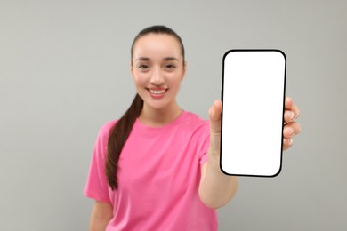 Photo of Young woman showing smartphone in hand on light grey background, selective focus. Mockup for design
