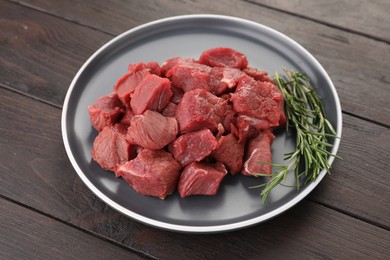 Pieces of raw beef meat with rosemary on wooden table