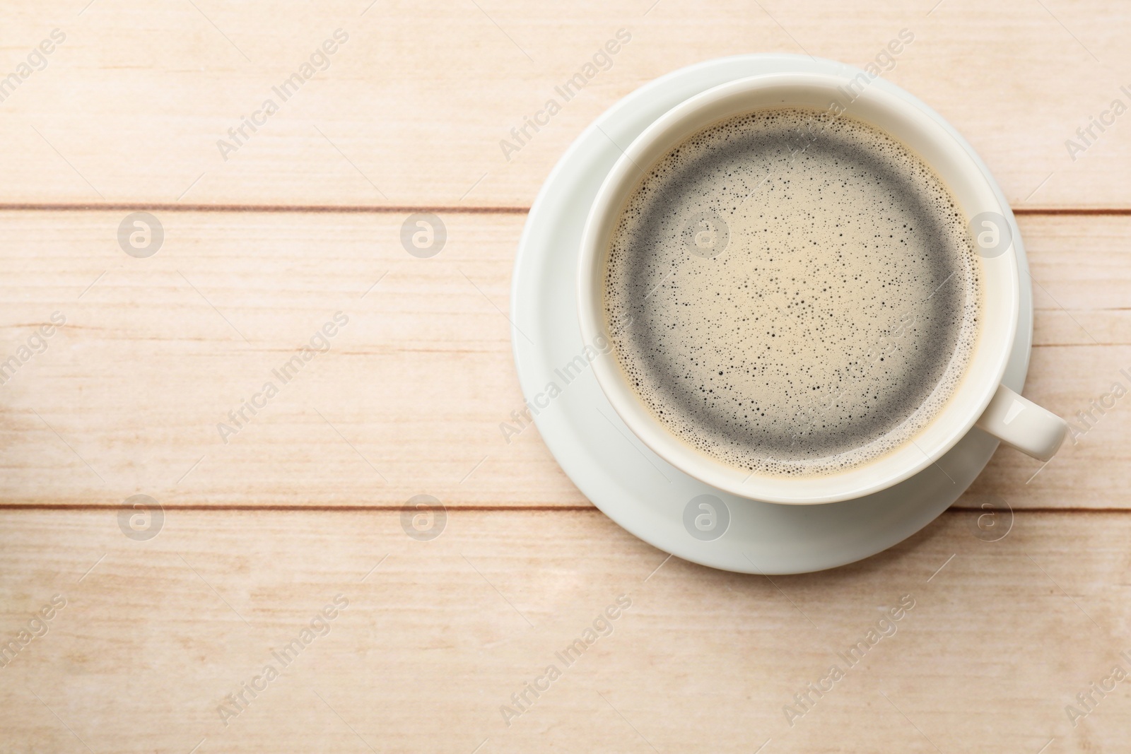 Photo of Cup of aromatic coffee on light wooden table, top view. Space for text