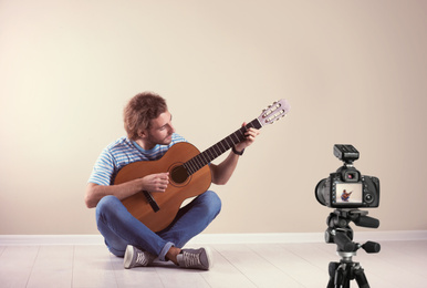 Image of Music teacher recording guitar lesson near beige wall