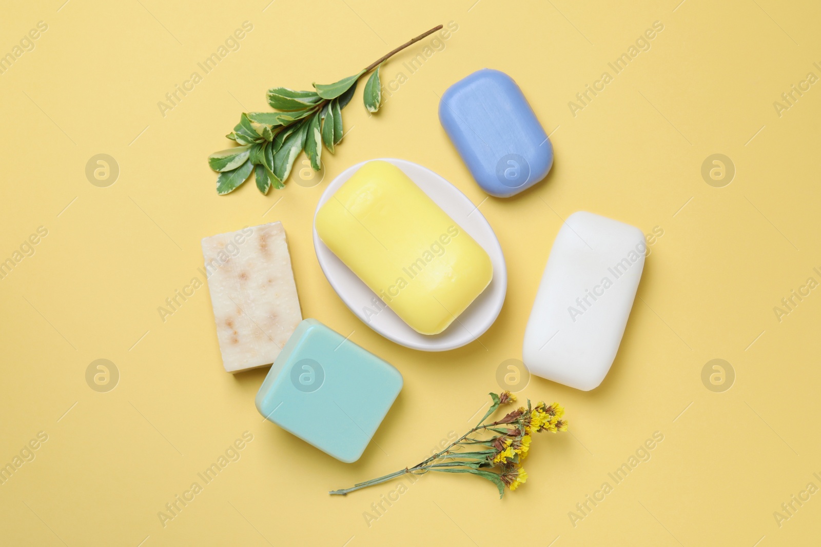 Photo of Many soap bars and plant branches on yellow background, flat lay