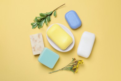 Many soap bars and plant branches on yellow background, flat lay
