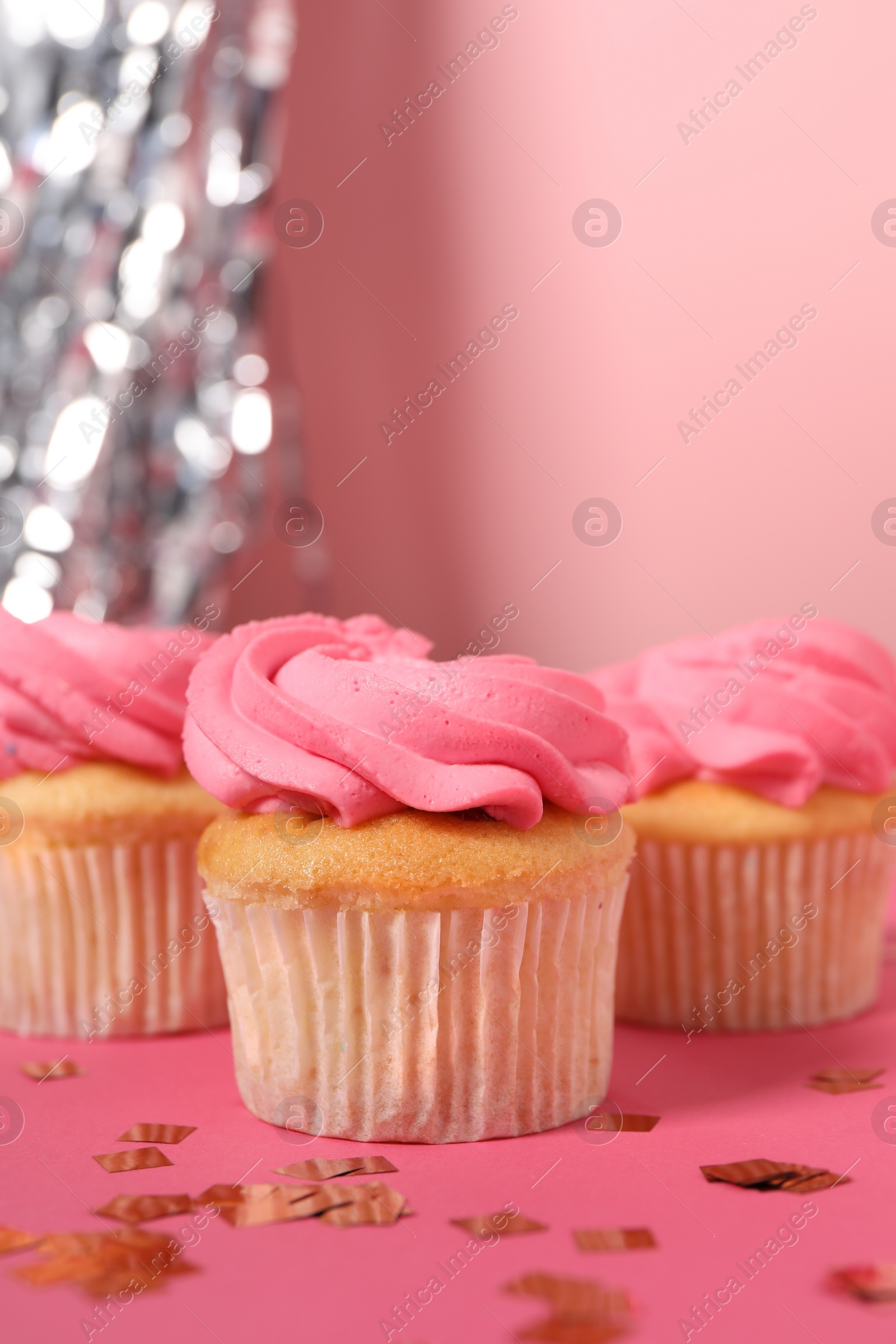 Photo of Delicious cupcakes with bright cream and confetti on pink background