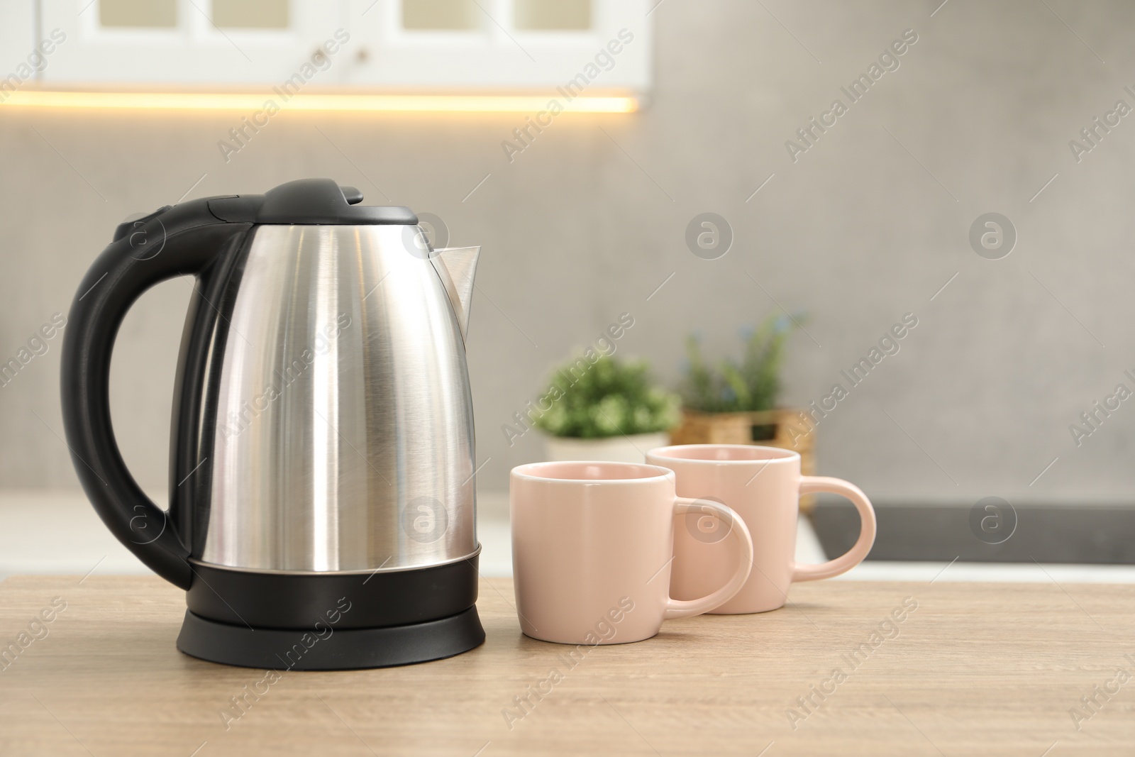 Photo of Modern electric kettle and cups on table in kitchen. Space for text