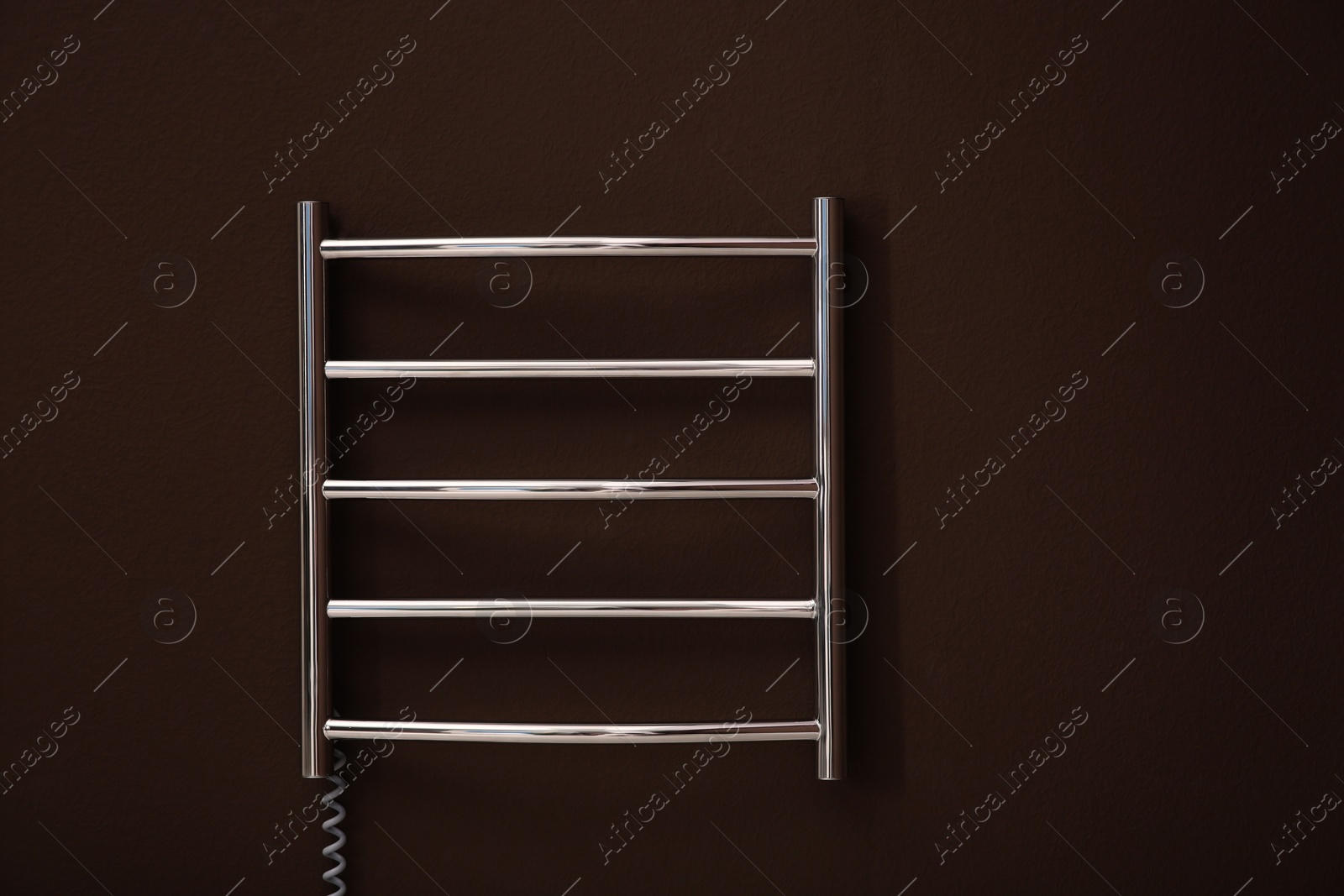 Photo of Modern heated towel rail on brown wall. Space for text